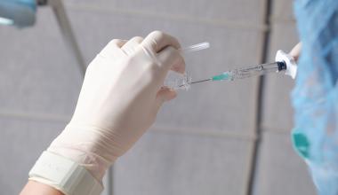 Gloved hands preparing a syringe by drawing liquid from a small vial.