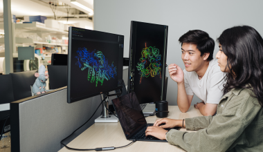Brian Hie and Aditi Merchant examine a protein structure generated by Evo 2, an AI tool that can suggest genome designs. Lab tests of Evo 2’s designs for an E. coli killer exceeded expectations. | Andrew Brodhead